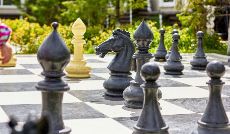 Giant chess set with figures and checkered board placed on ground in garden on sunny day